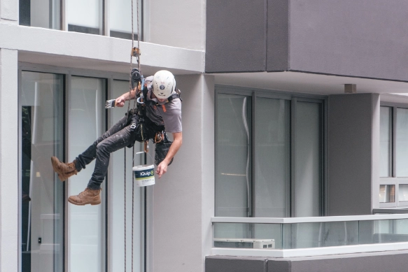 picture of a construction worker suspended mid-air painting the outside of a tall building